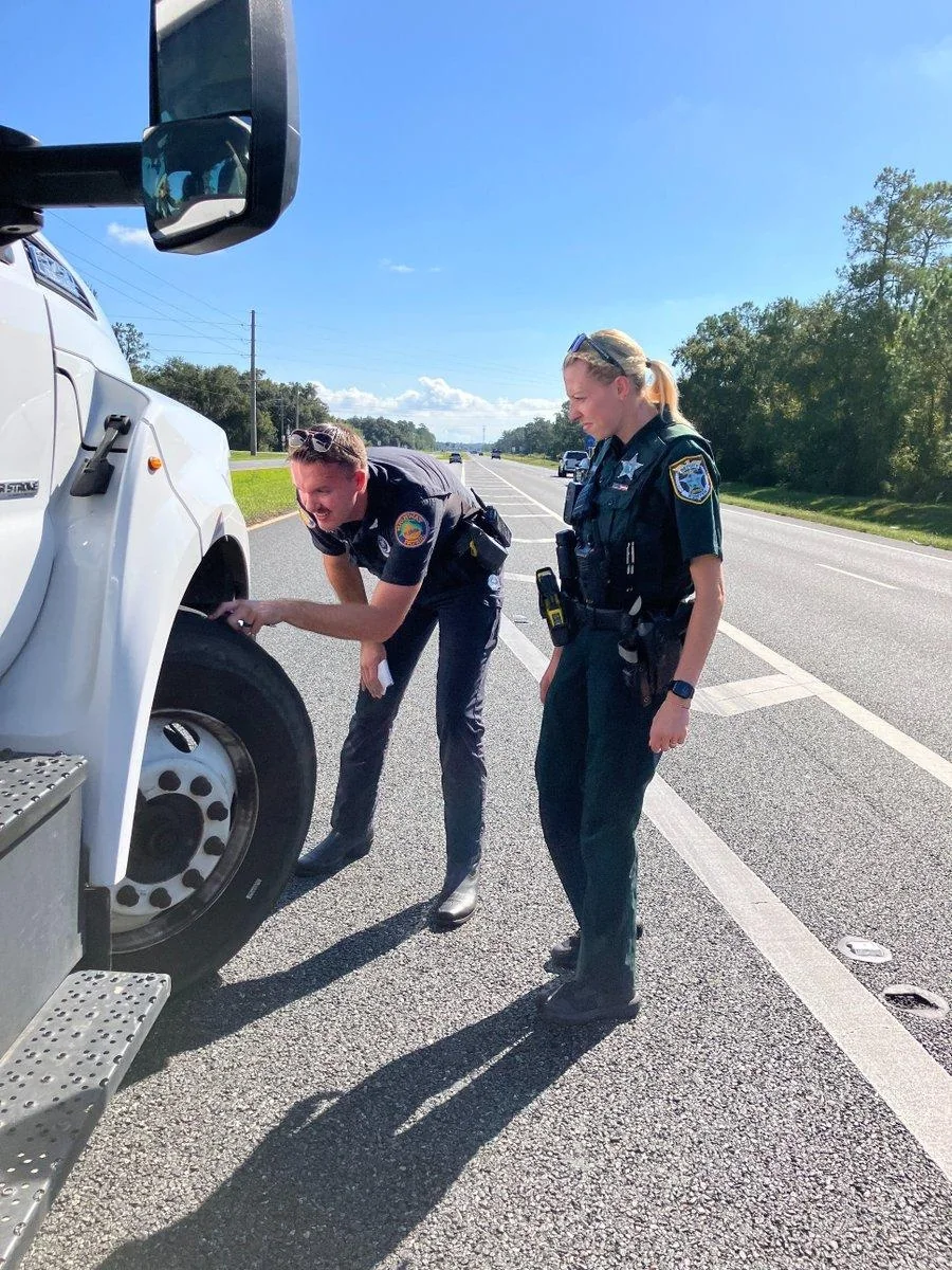 Two officers inspecting the front tire of a commercial truck